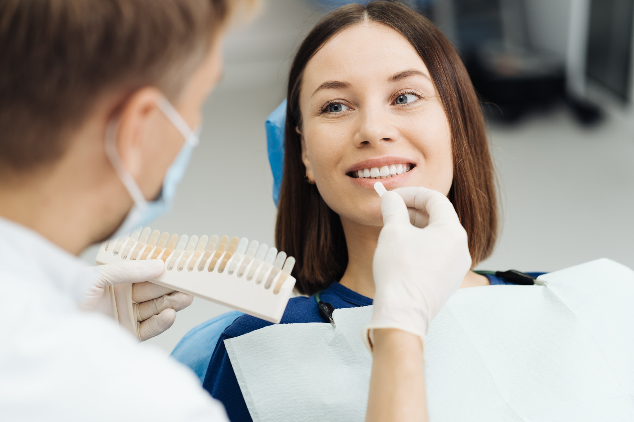 Dentist checking and selecting color of young woman’s teeth